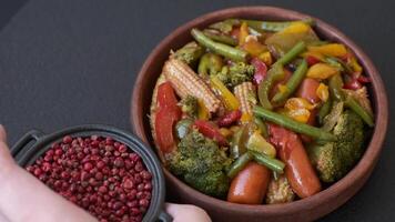 Mix of vegetables corn, carrots, peppers, broccoli, onions in teriyaki sauce on a ceramic plate on a dark concrete background video