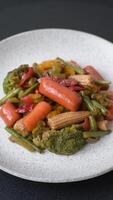 Mix of vegetables corn, carrots, peppers, broccoli, onions in teriyaki sauce on a ceramic plate on a dark concrete background video