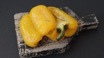 Yellow sweet pepper cut in half and grilled with salt, spices and herbs on a dark concrete background video