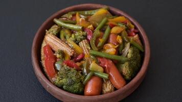 Mix of vegetables corn, carrots, peppers, broccoli, onions in teriyaki sauce on a ceramic plate on a dark concrete background video