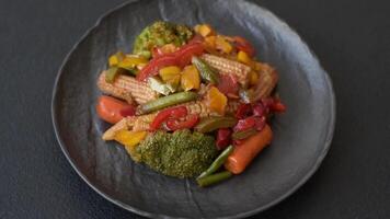 Mix of vegetables corn, carrots, peppers, broccoli, onions in teriyaki sauce on a ceramic plate on a dark concrete background video