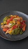 Mix of vegetables corn, carrots, peppers, broccoli, onions in teriyaki sauce on a ceramic plate on a dark concrete background video
