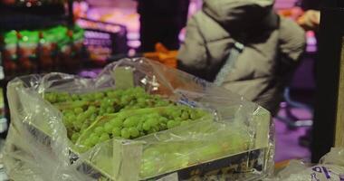 Green grapes in wooden boxes in a supermarket hall with shoppers in their carts in the background video