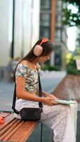 A Young Woman is Happily Enjoying Her Favorite Music While Reading Outside in a Beautiful Setting video