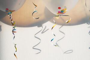 Balloons with colorful confetti and ribbons casting shadows on a wall. Celebration concept photo
