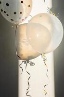 Two transparent balloons with colorful confetti, lit by sunlight and casting shadows. photo