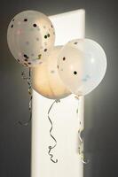 Two transparent balloons with colorful confetti, lit by sunlight and casting shadows. photo