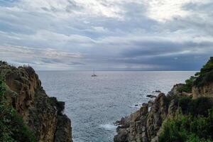 Sailboat on Serene Sea Between Rocky Cliffs Under Cloudy Sky - Nature Scene for Tranquility and Escape photo