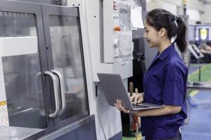 Asian woman industrial engineer wearing uniform using laptop control automated machine in industrial workshop. photo