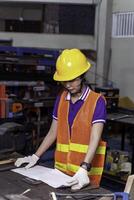 Asian woman technician Engineer in vest and helmet look and checking paper work at industrial workshop. photo