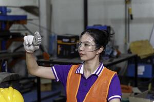 Closeup Asian woman industrial engineer looking an example small gear to check for completeness in industrial workshop. photo