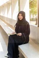 A cheerful and beautiful Muslim students wearing traditional clothes are intently reading Quran in the school building during breaks time in university. photo