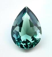 Sparkling teal gemstone in a tear drop shape illuminated by soft light showing intricate cuts and reflections on photo
