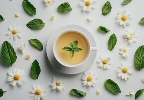 Herbal tea served in a white cup surrounded by fresh mint leaves and daisies on a clean surface in a bright and photo