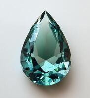 Sparkling teal gemstone in a tear drop shape illuminated by soft light showing intricate cuts and reflections on photo