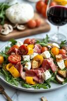 Colorful salad with fresh vegetables, prosciutto, mozzarella, and a glass of red wine served on a marble table photo