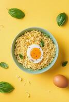 Delicious bowl of seasoned noodles with fresh basil and boiled eggs on a vibrant yellow background ready to photo