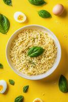 Delicious bowl of seasoned noodles with fresh basil and boiled eggs on a vibrant yellow background ready to photo
