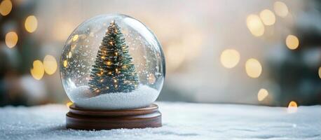 Christmas decorations featuring a small tree with lights and a snow globe filled with snowflakes and sparkles in photo