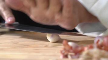 the chef expertly presses the sharp blade of their knife against the plump, golden shallots, carefully dicing them on a rich, light wooden brown cutting board. video