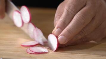 Slicing Radis on a wooden cutting board into slice pieces with a kitchen knife by professional chef. video