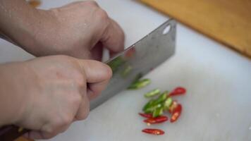 Asian hand slices red and green chilli by machete chopping knife on the plate in the kitchen. video