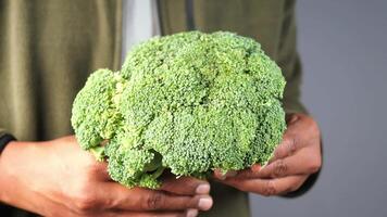A bunch of fresh broccoli held in hands against a simple, neutral background video