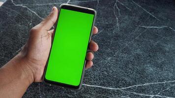 A hand holds a smartphone with a prominently displayed green screen video