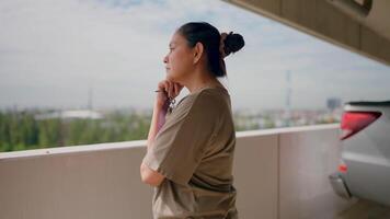 Contemplation on the Rooftop. A pensive woman gazes out from a rooftop parking garage, lost in thought. The urban landscape stretches behind her, adding depth and context to her contemplative mood. video
