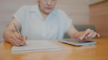 Focused and Productive. Hands of a woman taking notes, the tablet beside her on a table, a close-up shot capturing the essence of diligence and dedication. video