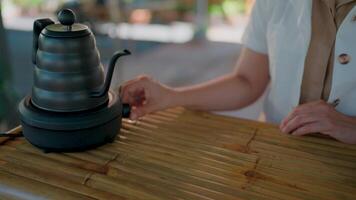 Brewing Tranquility. A close-up shot of a person hand gently turning on a stylish, dark-colored electric kettle resting on a bamboo surface, creating a serene and calming atmosphere. video