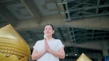 Finding Inner Peace. A woman in a white shirt stands in front of a golden structure with her hands clasped in prayer, evoking a sense of calm and serenity. video