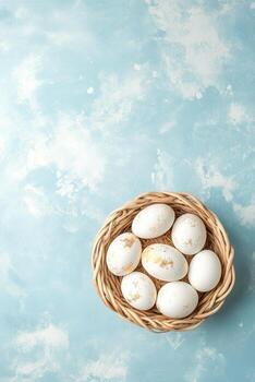 Freshly collected eggs nestled in a straw filled nest against a soft blue background photo