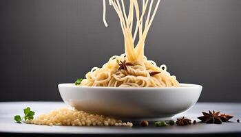 A bowl of noodles with a few strands falling in the air, a few star anise and a small parsley leaf in the foreground photo