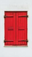 Bright red wooden shutters on a white wall in a sunny outdoor setting photo