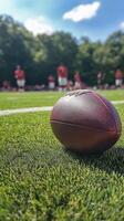 Football resting on field with players practicing in background during sunny day photo