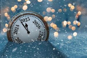 Vintage clock in the snow and points to the new year 2025. Beautiful winter background with golden lights bokeh at evening. New Year and Christmas Countdown, creative idea. photo