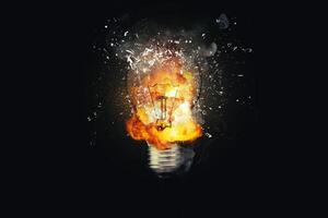 Creative light bulb explodes with fire with fragments and smoke on a black background, concept. Think differently creative idea concept. Dry paint splatter. Brainstorm and think photo