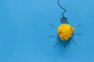 Inspiration concept crumpled paper light bulb metaphor for good idea. Yellow crumpled paper light bulb drawn on a blue background. Brainstorm and creative idea, concept. Project and startup photo
