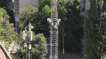 Mountaineering construction worker descends from 5G tower structure on roof of building. Speed up from top to basement of tower mast structure. Industrial mountaineering works on rooftop video