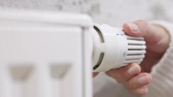 The woman turns off the heating by setting the thermostat of the central heating radiator to the minimum mode of maintaining the temperature in the room video