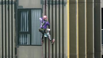 Workers painting the walls facade of a modern structure, demonstrating safety and precision in their task. video