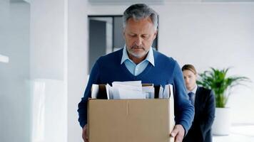 infeliz mayor empleado participación personal artículos en un caja después siendo puesto apagado, con un preocupado compañero de trabajo oficina trabajador que lleva personal en el antecedentes video