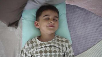 A little boy with dark short hair in pajamas wakes up and stretches his arms. slow motion video