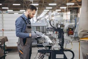Factory worker taking notes while operating industrial machinery for aluminum window frames photo