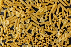 Different kinds of raw pasta texture on black background. photo