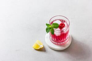 Raspberry cocktail with ice in a glass on a light background photo
