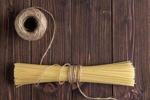 Raw pasta spaghetti with packthread and copy space on wooden background. photo