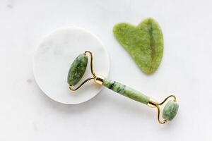 Green jade roller massager for face on white marble. photo