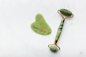 Green jade roller massager for face on white marble. photo